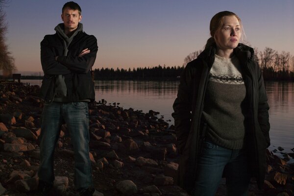 A man and a woman stand by the river at sunset