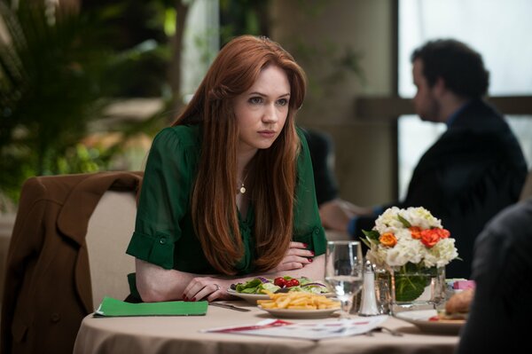 A red-haired girl in a green dress at a table in a cafe