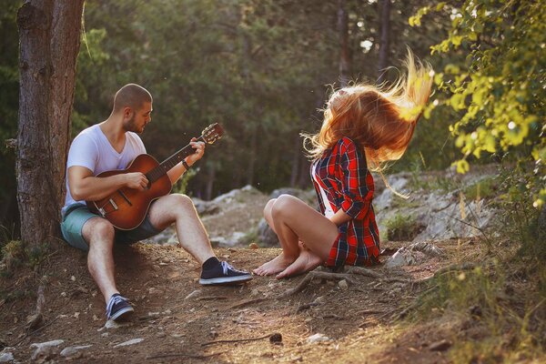 Un chico toca la guitarra junto a una chica en el bosque