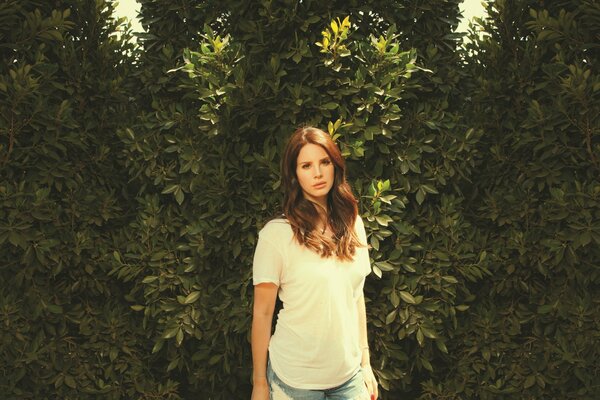 Singer Lana del Rey stands in a T-shirt against the background of bushes