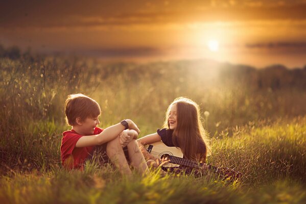 A boy and a girl are sitting and laughing in the grass, and deaochka is playing the guitar