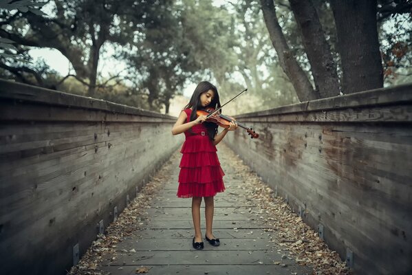 A violinist girl in a red dress plays outside