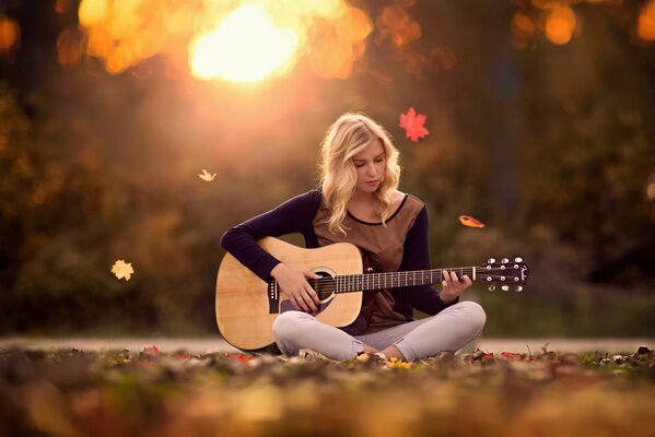 Schönes Mädchen mit einer Gitarre auf einem Hintergrund aus Laub