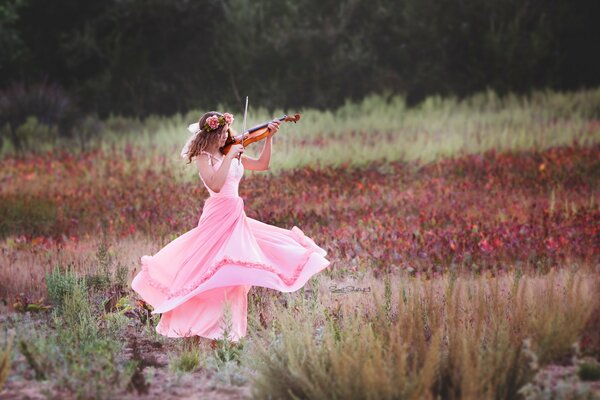 In the field, a girl in a pink dress is spinning and playing the violin