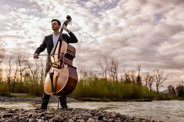 A man on the riverbank plays the double bass