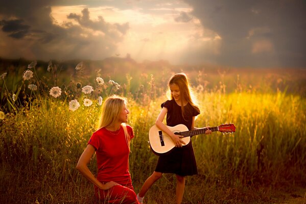 En el campo de verano, una niña toca la guitarra para su madre