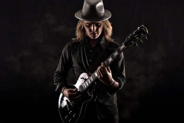 Jake Shepard in a black suit and a hat with a guitar