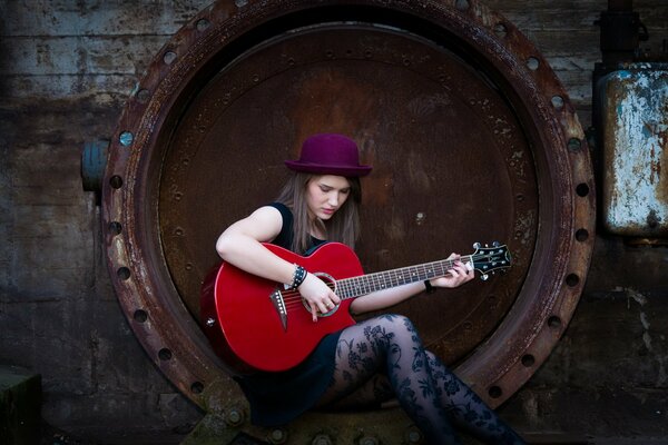 A girl plays a red guitar sitting in a rusty wheel