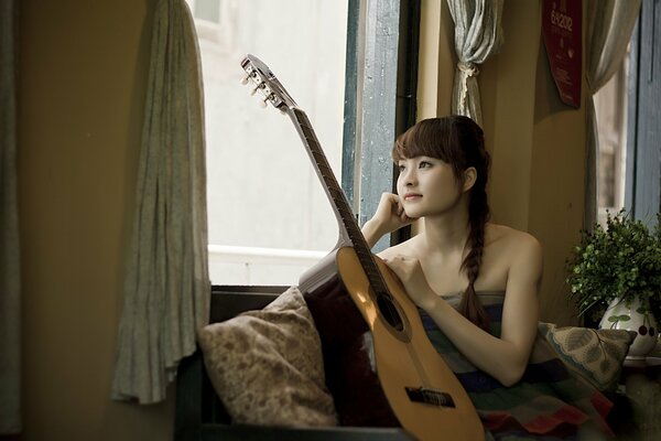 Mädchen sitzt mit Gitarre am Fenster