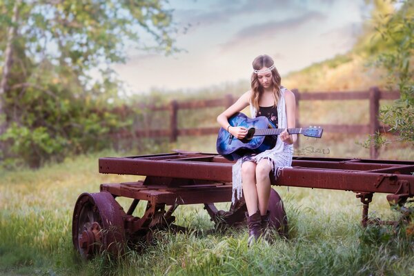 Sullo sfondo della natura, una ragazza suona la chitarra seduta su un carro