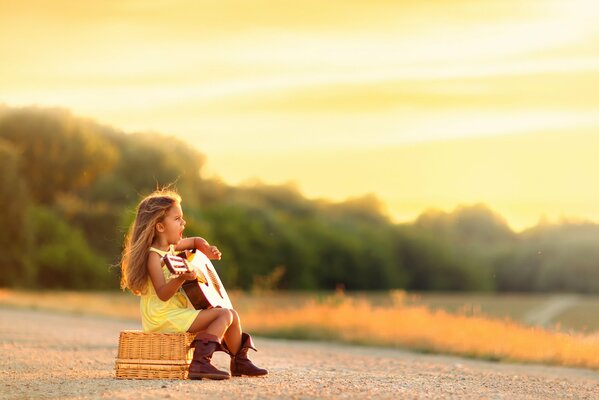 A little girl with a guitar on the road