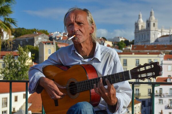 An aged man with a cigarette plays the guitar