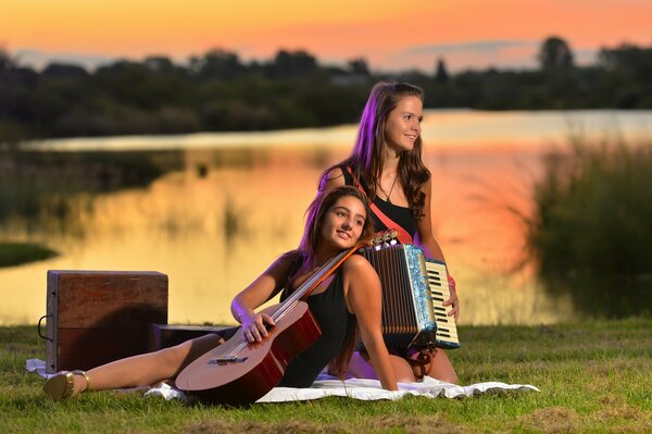 Two girls are sitting in a clearing with a guitar and an accordion