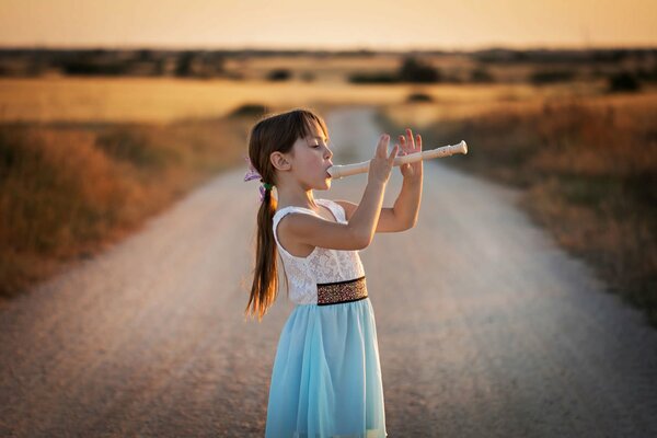 A girl on an empty road plays a pipe