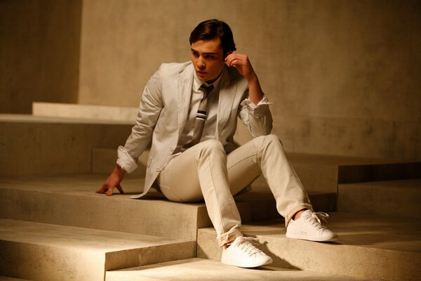 A guy in a white suit is sitting on the steps of a suit