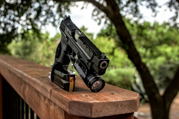 A pistol with a flashlight on the wooden railing