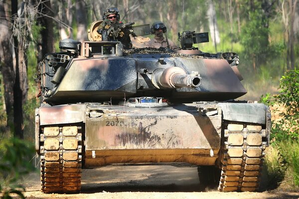 The tank is moving along a forest road and a man is visible on it