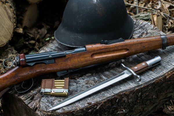 Auf dem Baumstumpf eine Reihe von Waffen. Bajonett-Messer, Gewehr, Helm