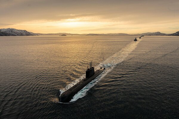 Submarines sail on the sea against the background of sunset