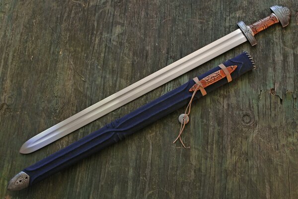 A sword with a scabbard lies on a wooden surface