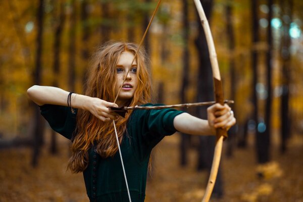 Chica con un arco en el fondo del bosque de otoño