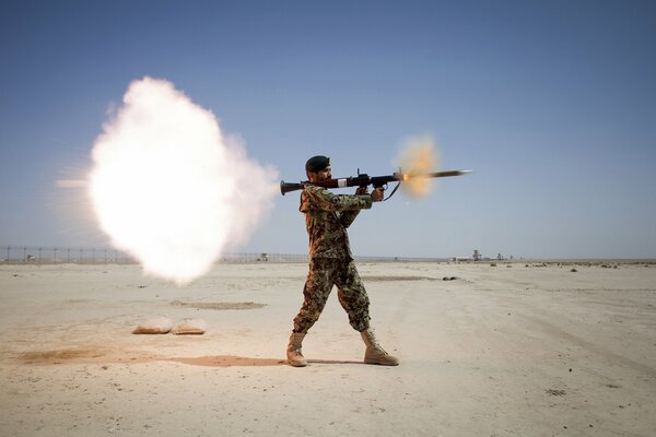 A soldier fires a grenade launcher in the desert