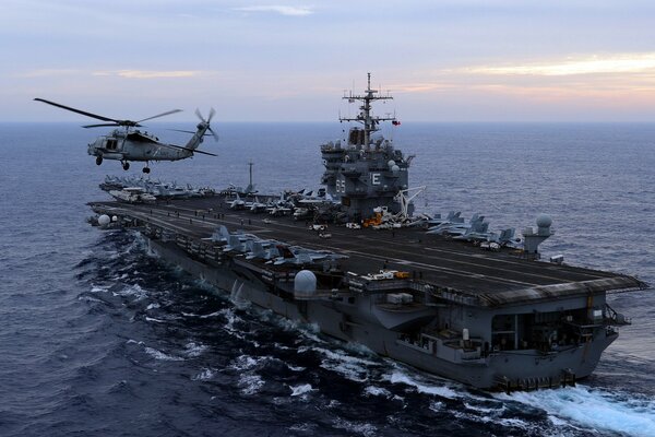 A military aircraft carrier with a helicopter at sea