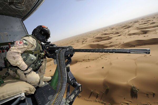 A soldier with a machine gun sitting in a helicopter on a desert background