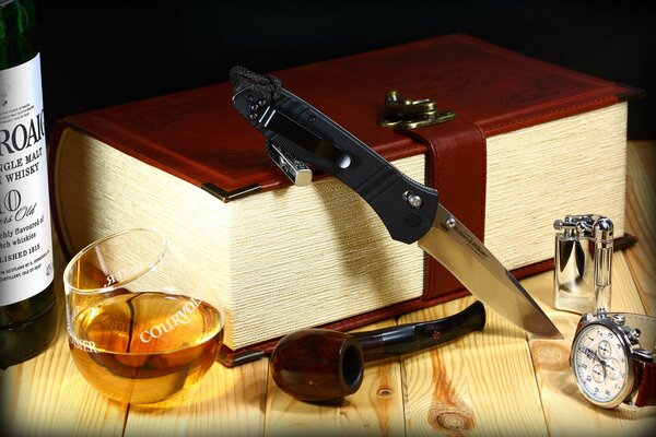 El cuchillo descansa sobre un libro grueso y hay un whisky con un tubo al lado