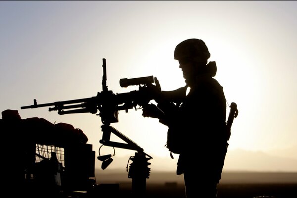 Silhouette of a soldier with a machine gun at sunset