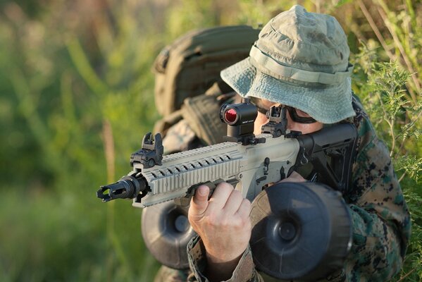 A man with a gun is sitting in the green bushes