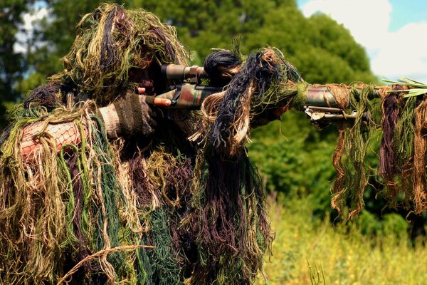 Sniper in camouflage under the grass with a machine gun