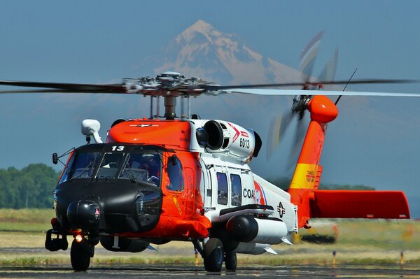 A helicopter takes off at the airfield against the background of a mountain