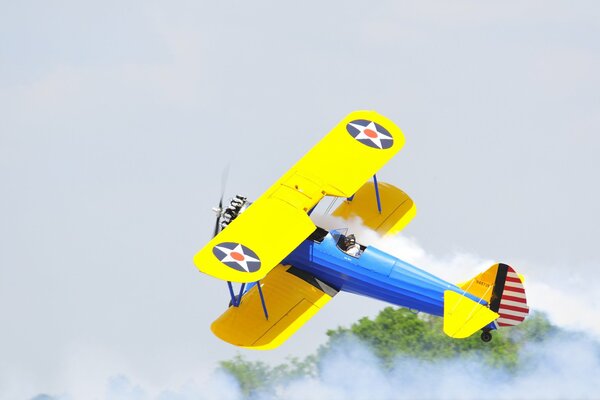 Un biplano amarillo y azul vuela en la niebla