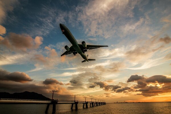 Flugzeug tief über Fluss und Brücke bei Sonnenuntergang