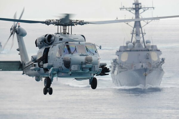 Sh - 60f Mehrzweckhubschrauber fliegt vor dem Hintergrund eines Kriegsschiffes