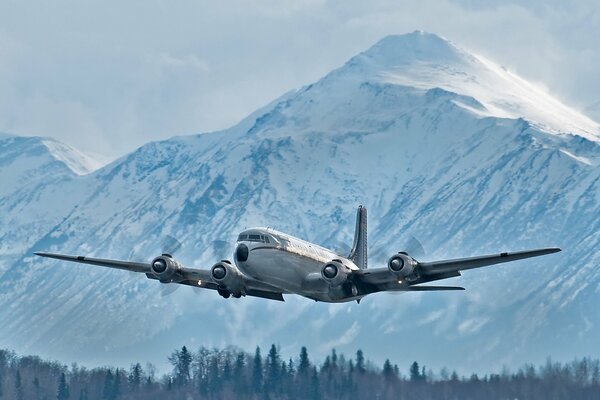 Militär-Transportflugzeug am Himmel vor dem Hintergrund eines schneebedeckten Berges