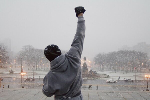 The guy is standing with his back raised his hand up, it s snowing, Pushkin Square