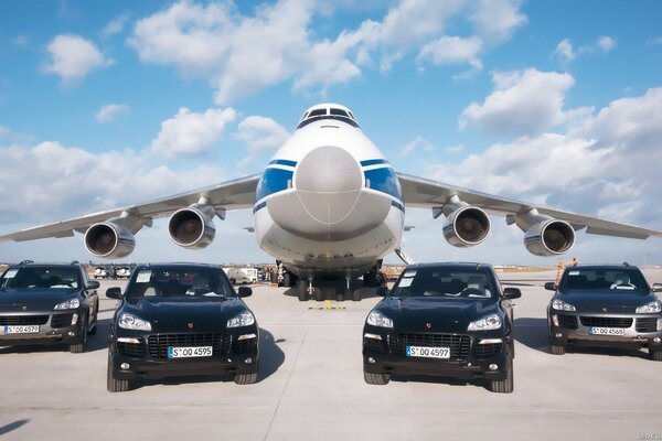 El avión de carga de Antonov en el aeropuerto rodeado de autos Porsche