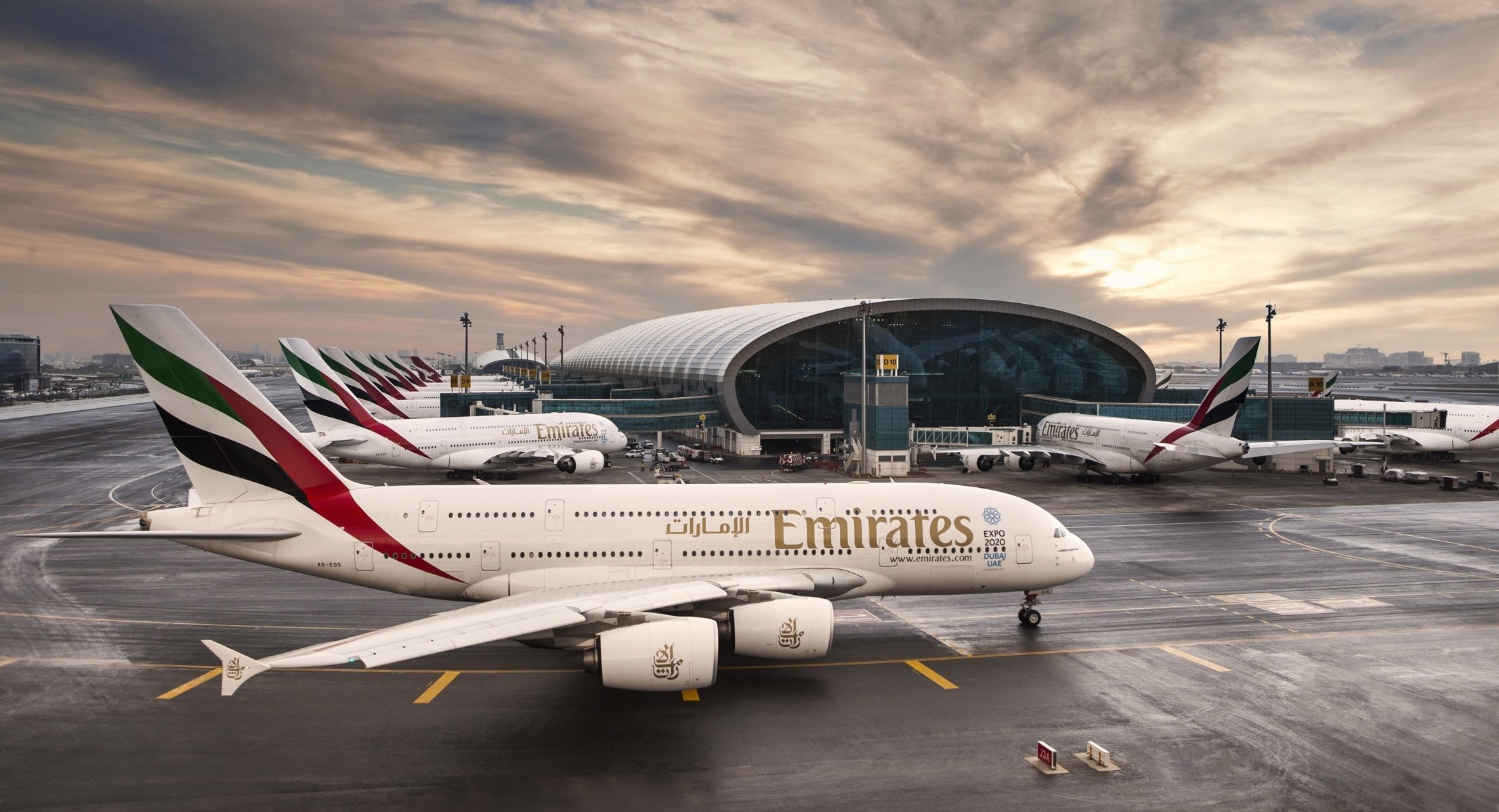 linie lotnicze emirates airbus a380 samolot pasażerski samolot pasażer lotnisko dubaj zjednoczone emiraty arabskie budynek terminal wschód słońca niebo chmury pasażer