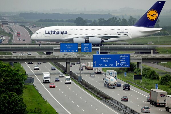 A white big plane is flying over the highway