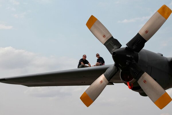 Two people are sitting high in the sky on the wing of an airplane