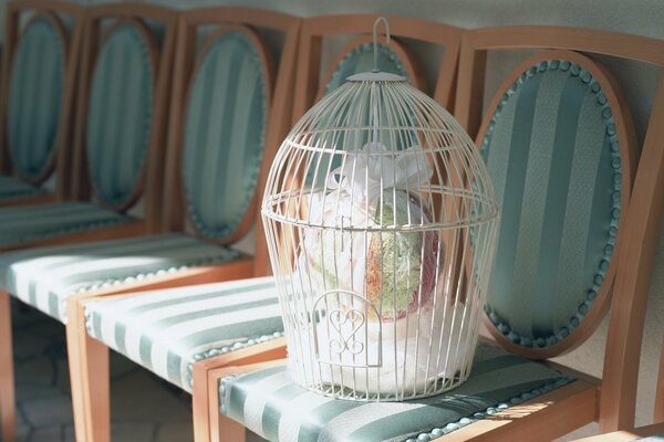 A white cage with a bouquet inside stands on a chair upholstered in green silk