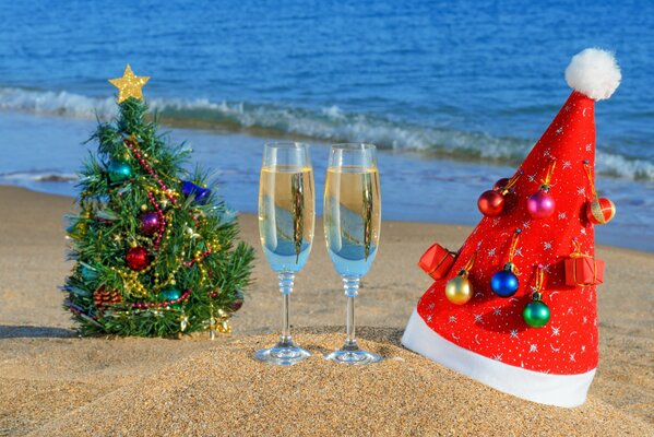 Christmas tree, Santa Claus hat and two glasses of champagne on the ocean beach