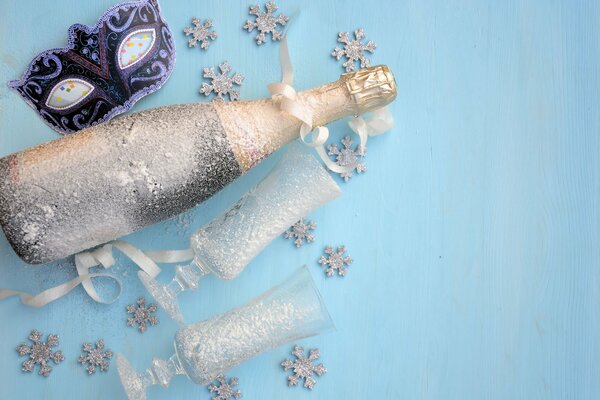 Une bouteille de champagne et deux verres de couleur argentée à côté d un masque de carnaval