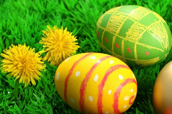 Two Easter eggs in the grass and two dandelions