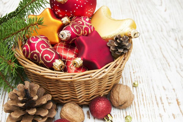 Juguetes de Navidad rojos y dorados en una canasta con conos y nueces en una tabla de madera