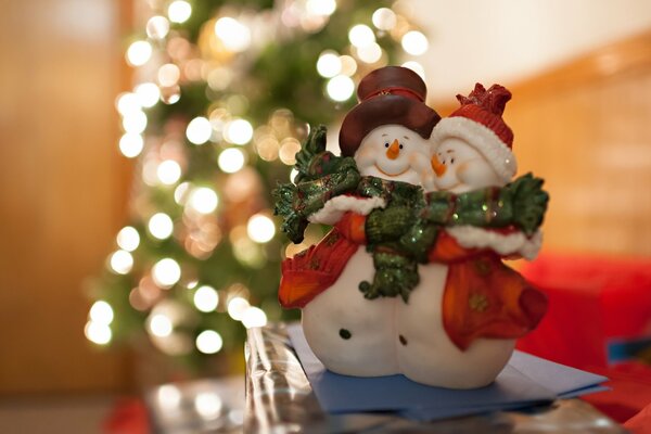 Un paio di pupazzi di neve soddisfatti sullo sfondo di un albero di Natale luminoso in lontananza