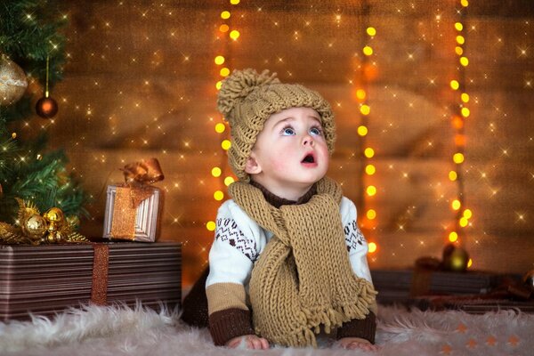 Bambino su sfondo di Capodanno in cappello e sciarpa guarda in alto