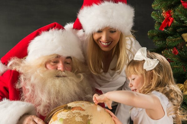 Der Weihnachtsmann hält eine Kugel, die von einer Frau und einem Mädchen betrachtet wird